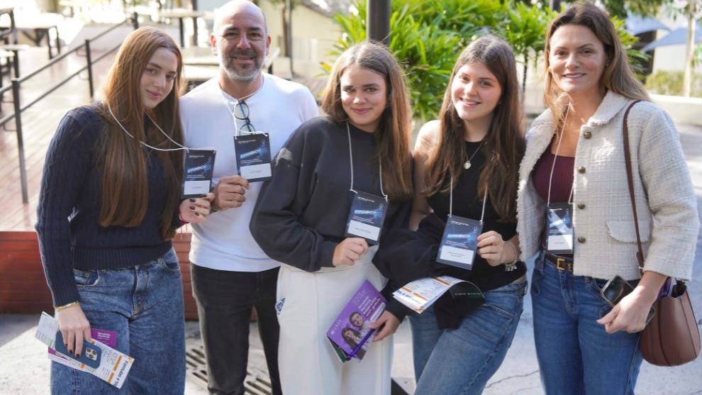 Grupo de cinco pessoas ao ar livre, sorrindo e exibindo crachás do Experiência FGV, com folhetos nas mãos e ambiente arborizado ao fundo.
