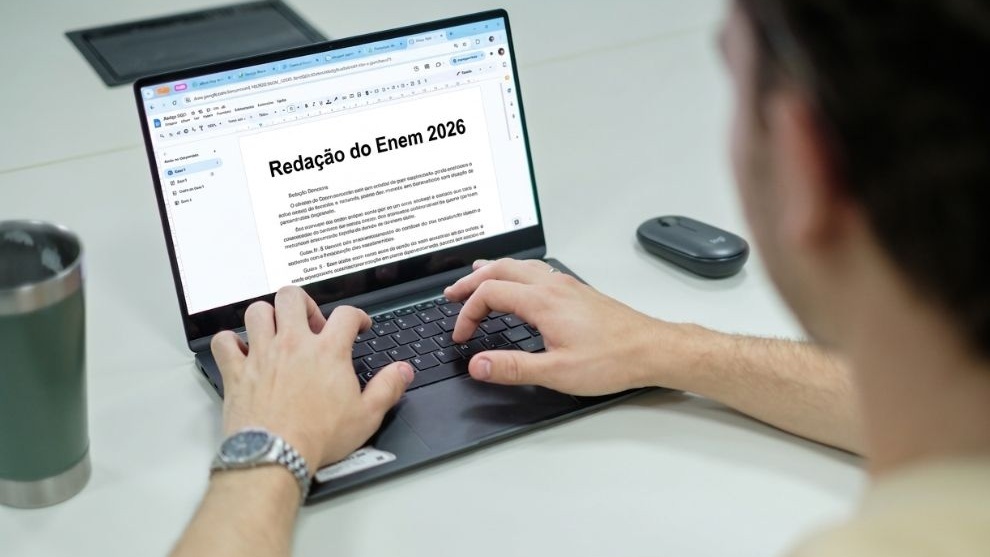 A imagem mostra uma pessoa digitando em um laptop, com o documento "Redação do Enem 2026" na tela.