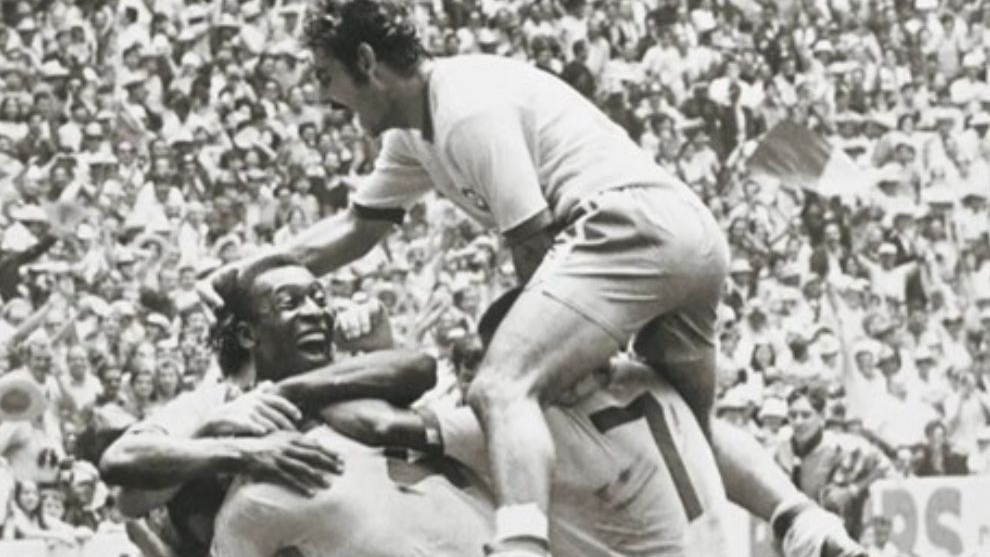 Jogadores de futebol comemoram em campo durante uma partida histórica da Copa do Mundo, com arquibancada lotada ao fundo.