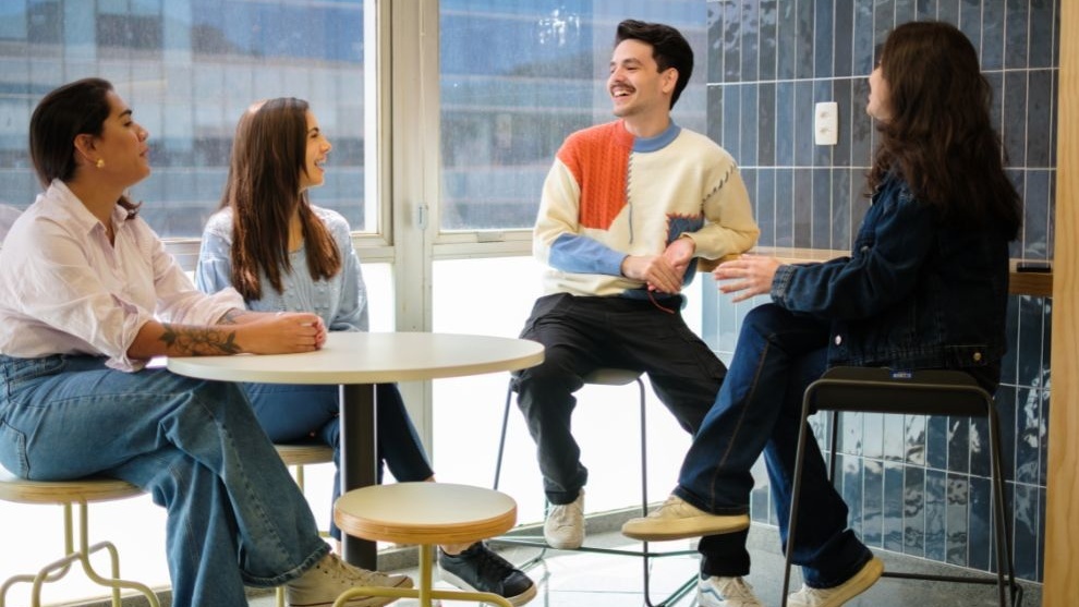 Quatro jovens em ambiente interno, conversando de forma descontraída.