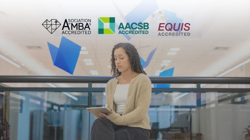 Estudante com tablet em ambiente moderno, sob os selos de acreditação AMBA, AACSB e EQUIS.