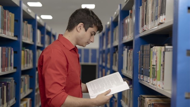 aluno em pé lendo livro na biblioteca