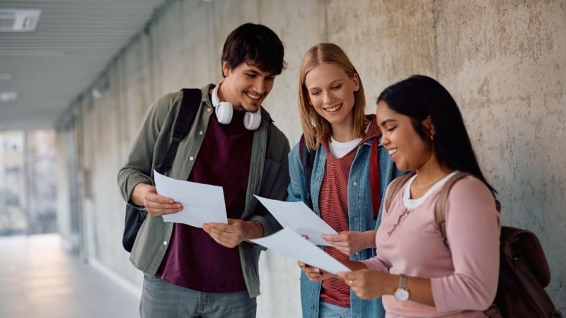 alunos em pé segurando papeis conversando