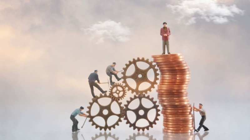 Miniaturas de trabalhadores ajustam engrenagens ao lado de uma pilha de moedas, com um homem no topo, simbolizando trabalho, economia e crescimento financeiro.