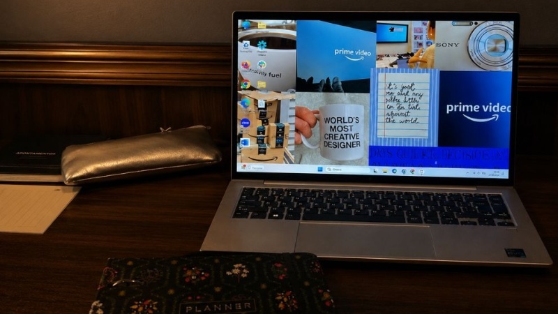 Notebook aberto sobre uma mesa de madeira, ao lado de um estojo prateado e um planner floral, em um ambiente de trabalho com iluminação aconchegante.