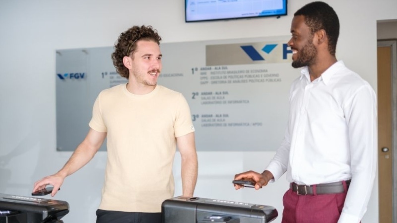 Dois estudantes conversam e sorriem enquanto passam pelas catracas de entrada de uma unidade da FGV.