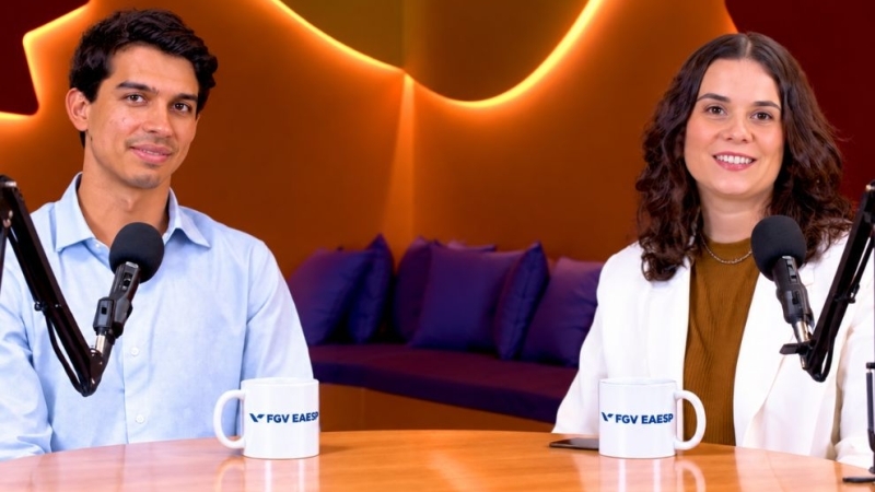 Duas pessoas em um estúdio de podcast, diante de microfones e canecas com a logo da FGV EAESP.