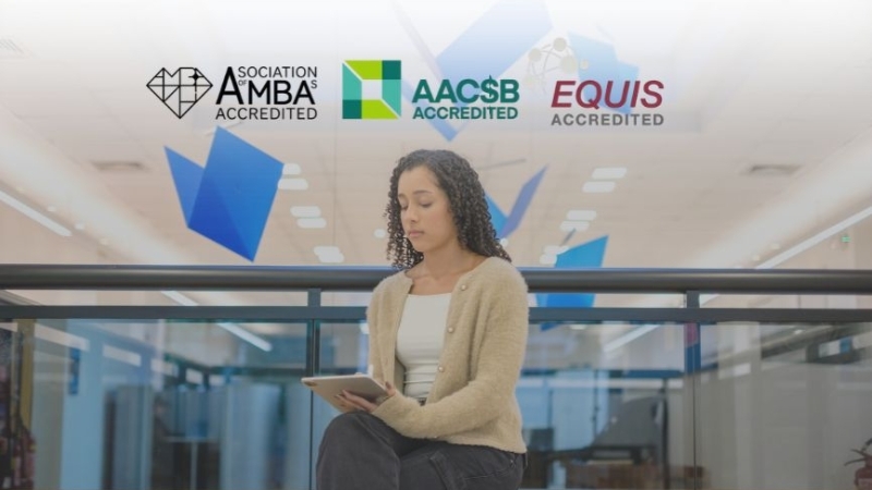 Estudante com tablet em ambiente moderno, sob os selos de acreditação AMBA, AACSB e EQUIS.
