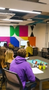 Sala de aula moderna com estudantes sentados em mesas usando computadores, em um ambiente colaborativo e colorido.