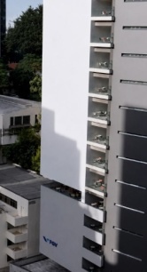 Vista externa de um edifício moderno da FGV em área urbana, com fachada branca e cinza, varandas envidraçadas e o logotipo da FGV visível na entrada.