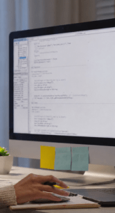 Pessoa trabalhando em um computador com código exibido na tela.