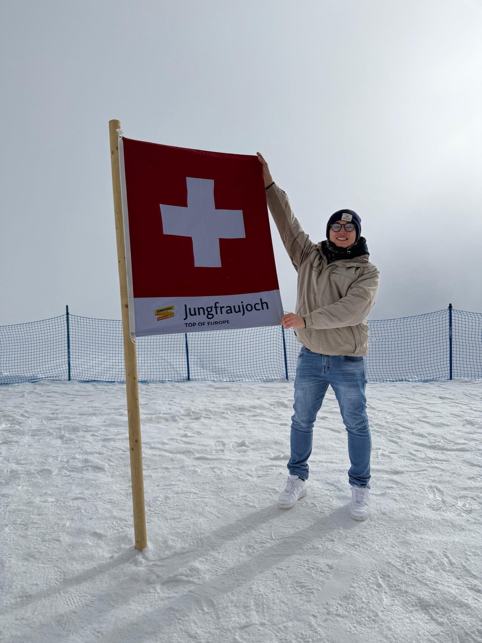 Rapaz na neve segurando uma bandeira da Suíça no topo de Jungfraujoch, usando roupas de inverno.